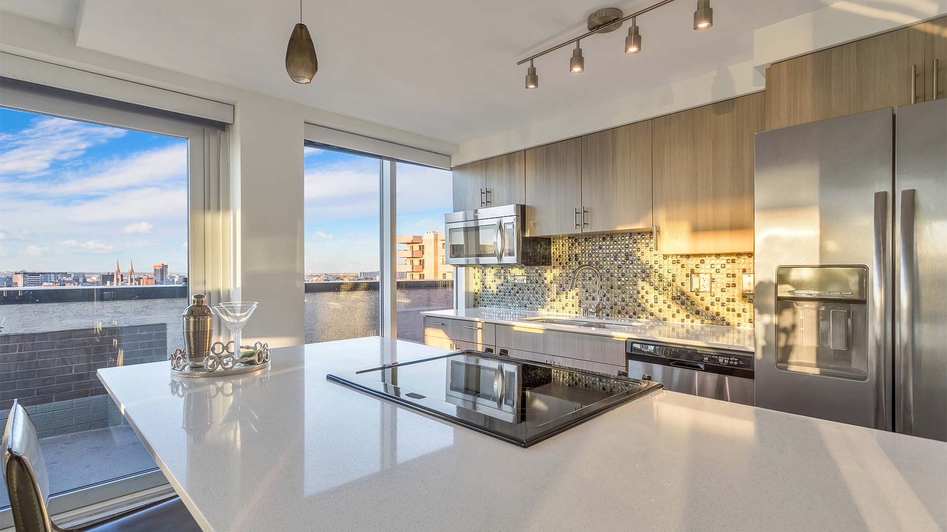 Kitchen with light counters, stainless steel appliances, wood cabinets, and large windows to balcony.