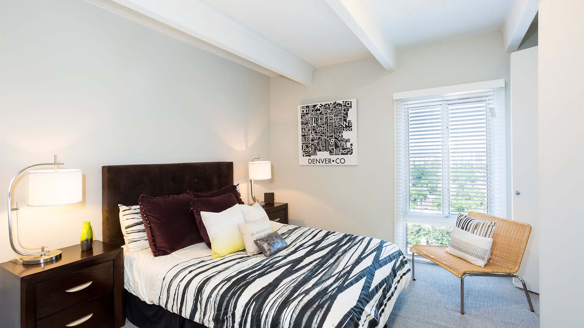 Bedroom with carpet, plush bed with headboard, bedside drawers with lamps, and large window.