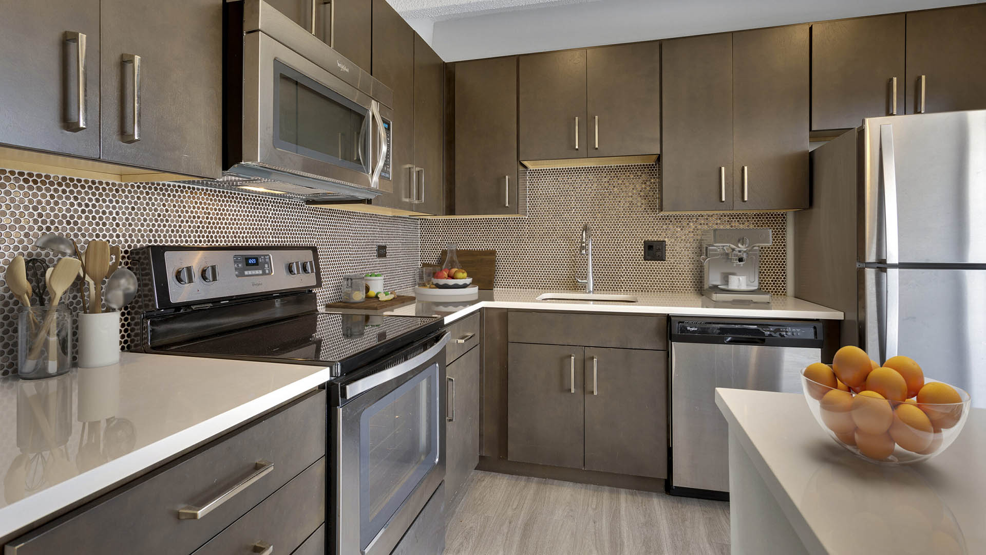 Kitchen with wood floor and cabinets, light counters, stainless steel appliances, and bowl of oranges.