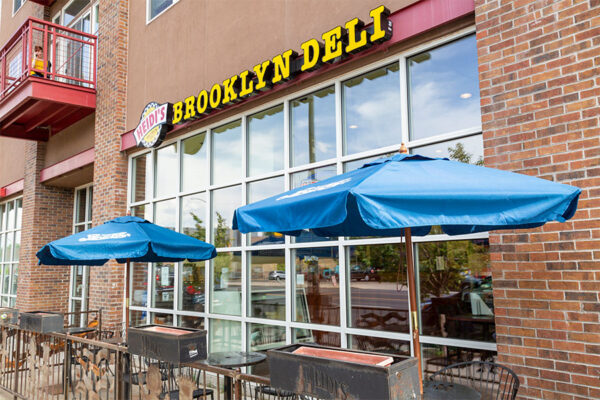 Heidi's Brooklyn Deli restaurant with glass wall and patio with umbrellas.