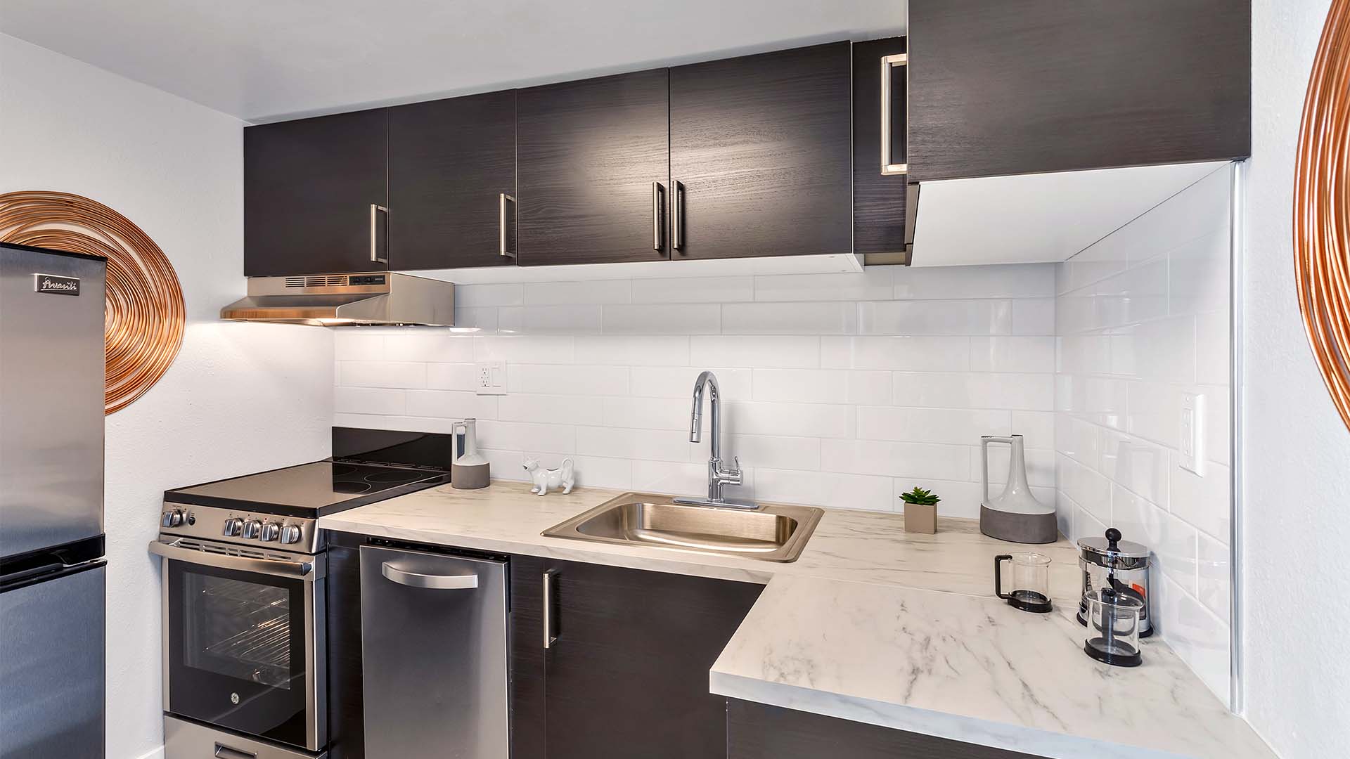 Kitchen with dark cabinets, stone counter, stainless steel appliances, and wall art.