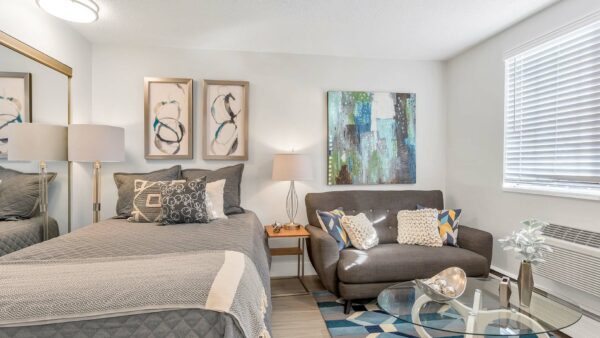 Studio apartment with plush bed, comfortable lounge seat, glass table, and wall art.