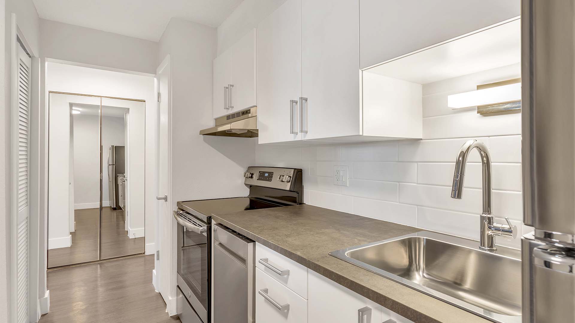 Kitchen with white cabinets, grey counters, stainless steel appliances, and pantry.