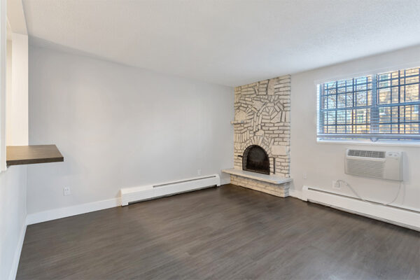 Living room with wood floor, white brick fireplace, and large window.