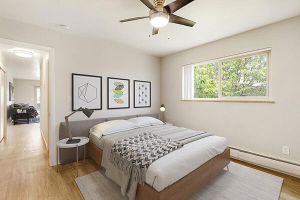 Bedroom with wood floor, large bed with padded headboard, bedside tables with lamps, and large windows.