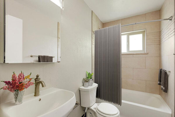Bathroom with tiled shower tub, round sink, large medicine cabinet, and decorative flowers.
