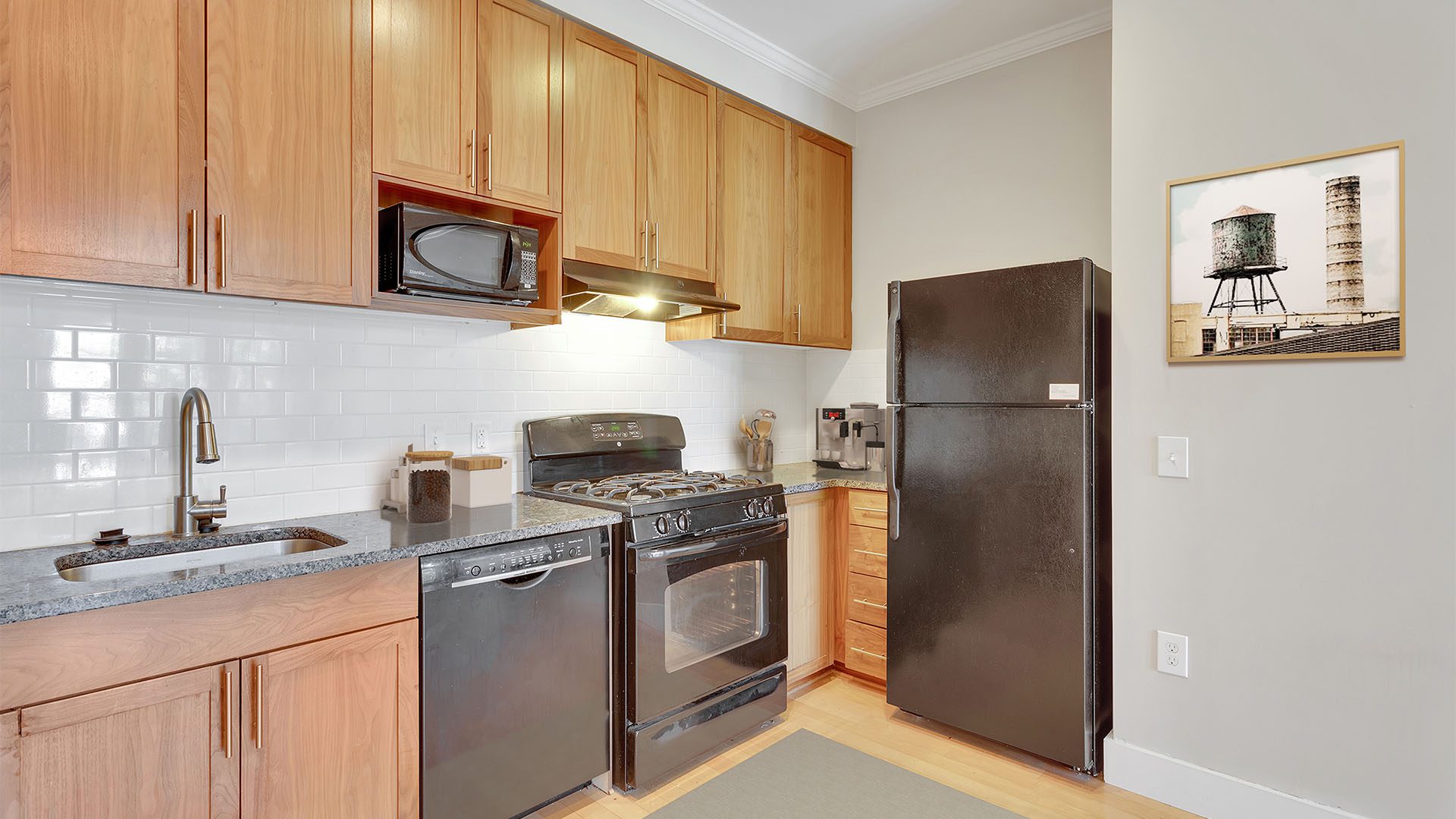 Kitchen with wood floor and cabinets, stone counters, black appliances, and tiled backsplash.