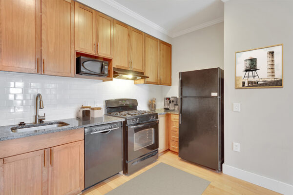 Kitchen with wood floor and cabinets, stone counters, black appliances, and tiled backsplash.