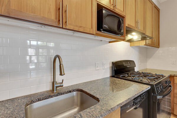 Kitchen with wood cabinets, stone counters, black appliances, and subway tile backsplash.