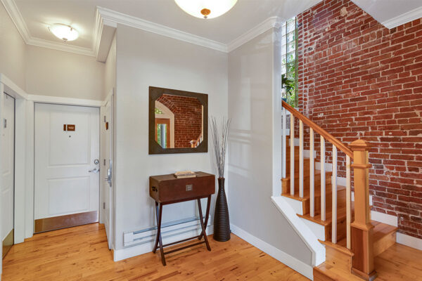 Stairway with wood treads, brick accent wall, and large window with potted plant.