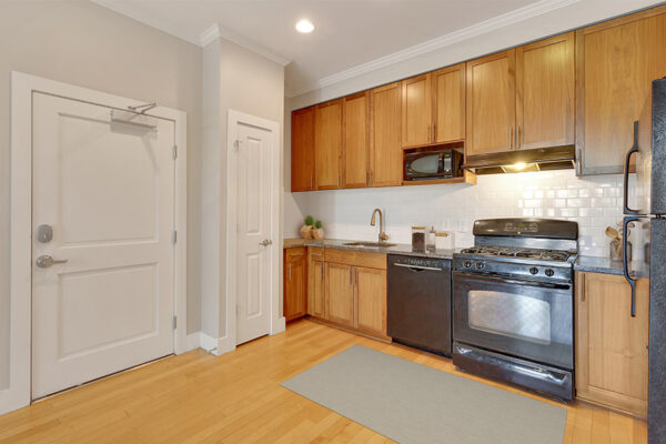 Kitchen with wood floor and cabinets, stone counters, and black appliances.