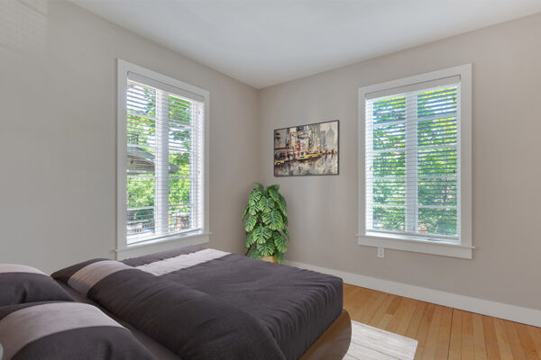 Bedroom with wood floor, plush bed, potted plant, and large windows.