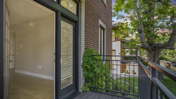 Balcony with metal railings, lush landscaping, and large door.