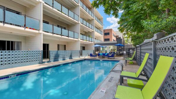 Pool area with lounge chairs and dining tables overlooked by apartment balconies.