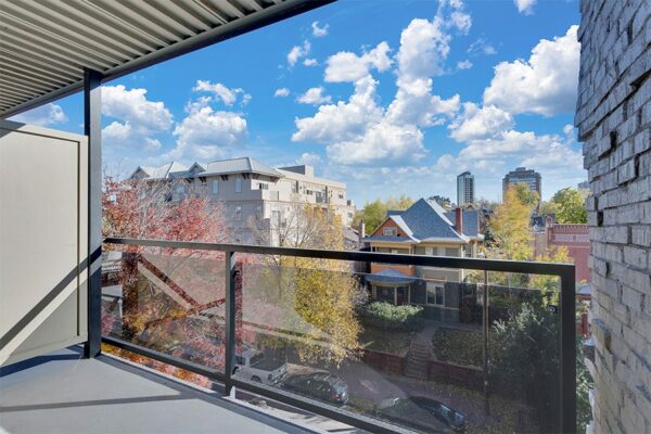 Balcony with metal and glass railing overlooking street with classic houses.