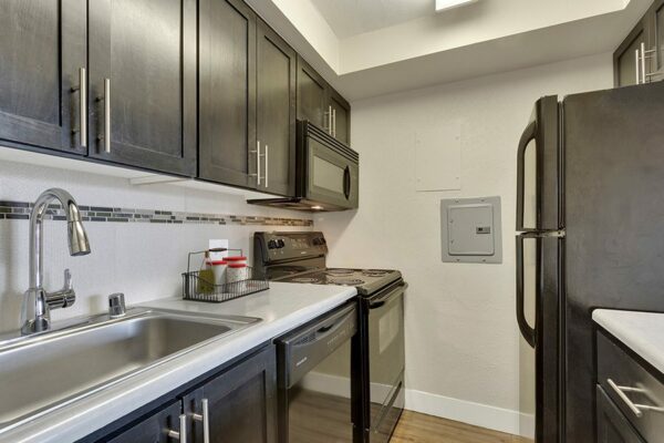Kitchen with wood cabinets, grey counters, black appliances, and tiled backsplash.