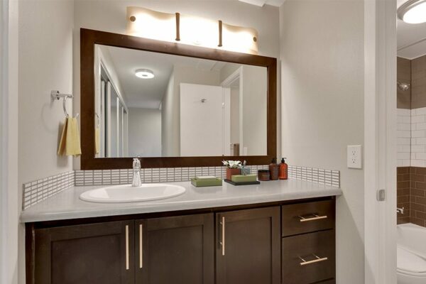 Bathroom with wood cabinets, grey counters, framed mirror, and eclectic lighting fixture.