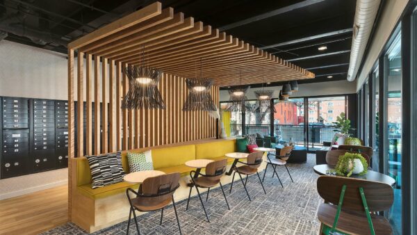 Lounge with decorative wood slats, booth with round tables and chairs, mailboxes, and glass walls.