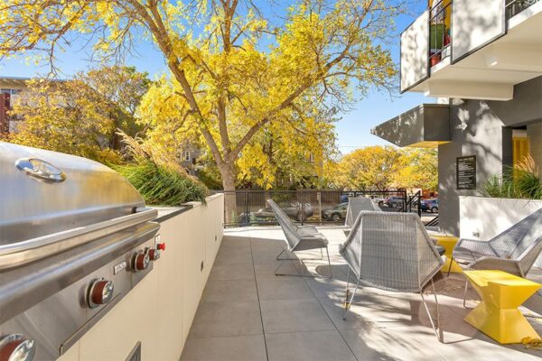 Outdoor lounge with seating, built in BBQ grills, and lush landscaping.