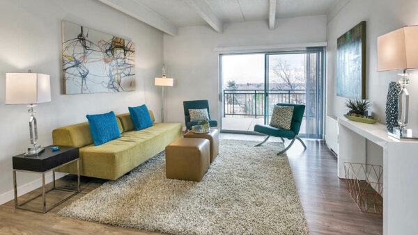Living room with wood floor, plush rug, modern furniture, large artwork, and door to balcony.