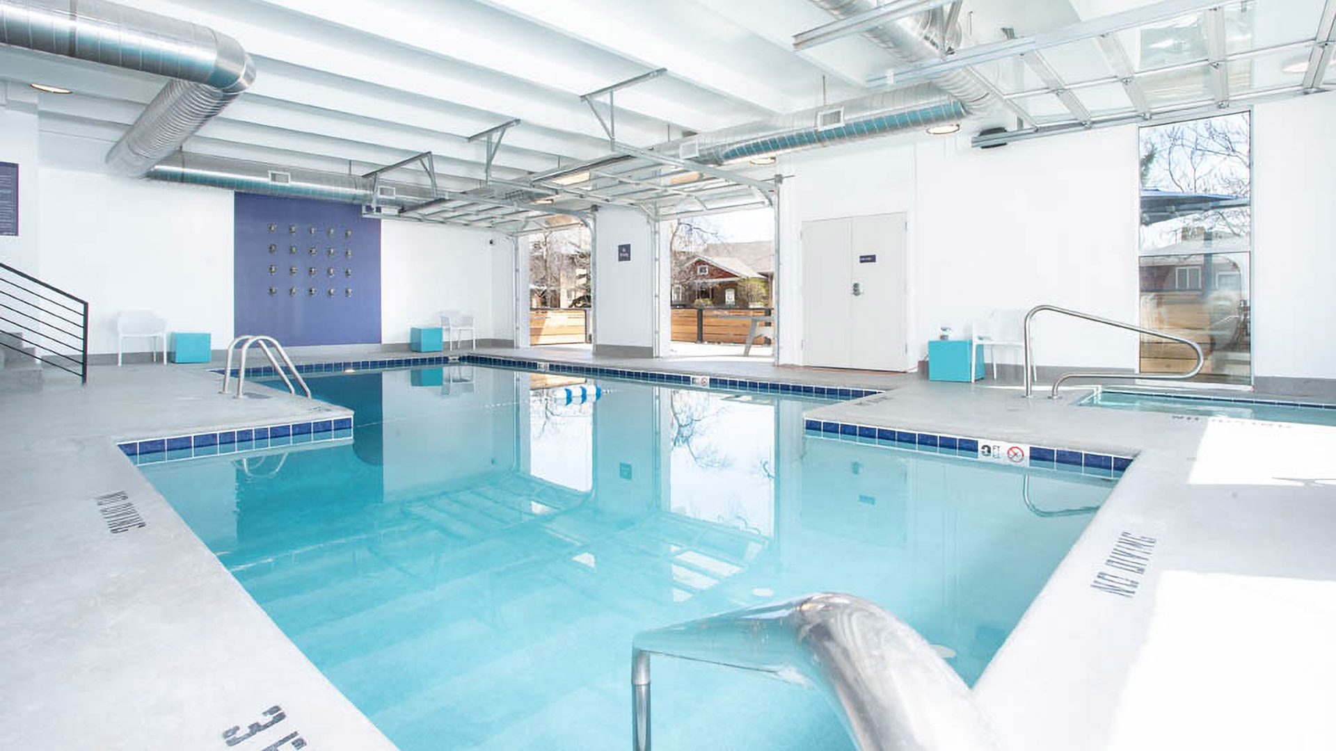 Indoor pool and spa with bright blue water and garage doors to patio.