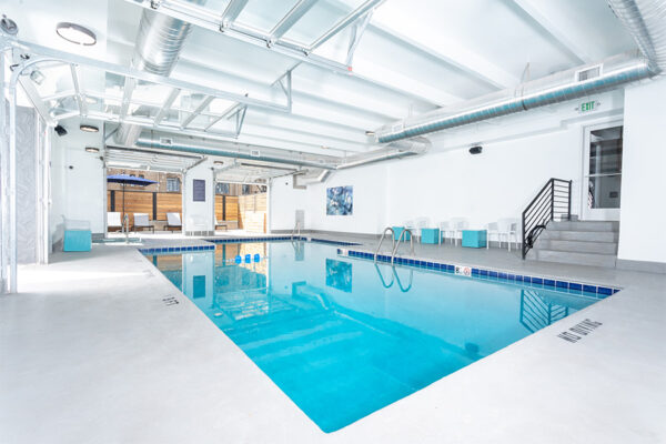 Indoor pool area with lounge chairs and garage doors to outside.