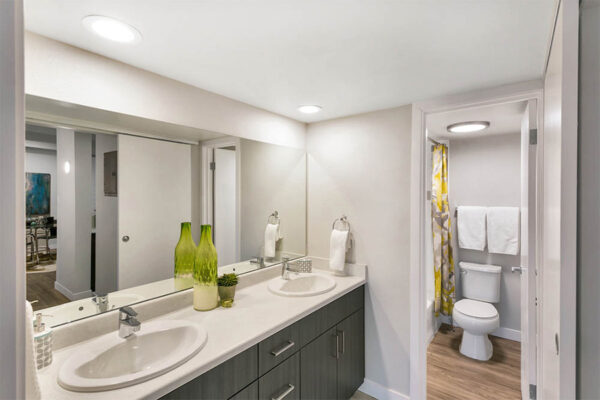 Bathroom with wood cabinets, light counters, large mirror, and decor.