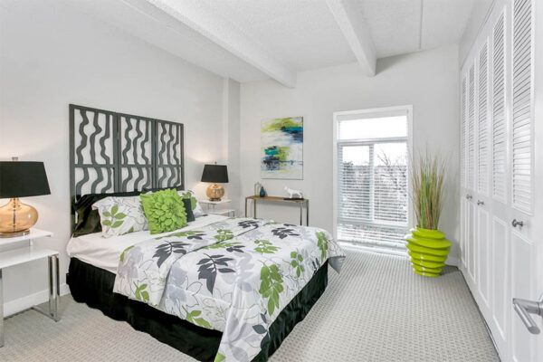 Bedroom with carpet, bed with plush bedding and decorative headboard, bedside tables with lamps, and large window.