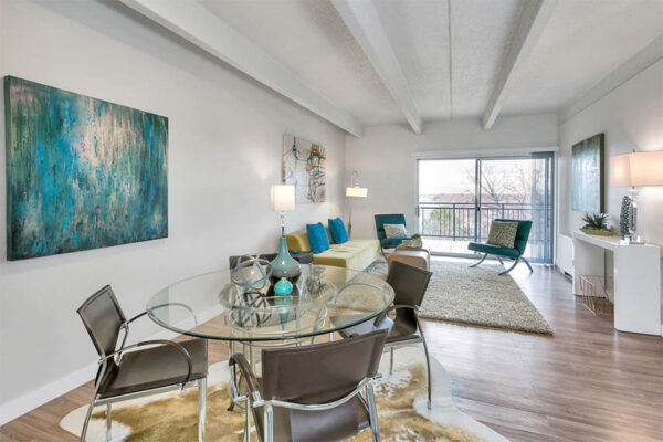 Living area with wood floor, large rugs, glass dining table, modern furniture, and door to balcony.