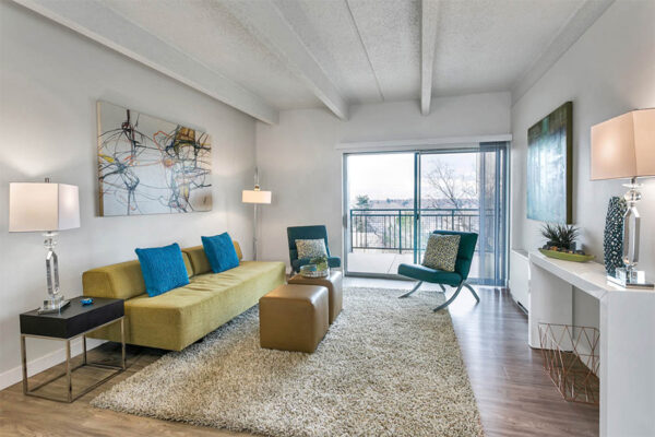 Living room with wood floor, plush rug, modern furniture, and sliding door to balcony.