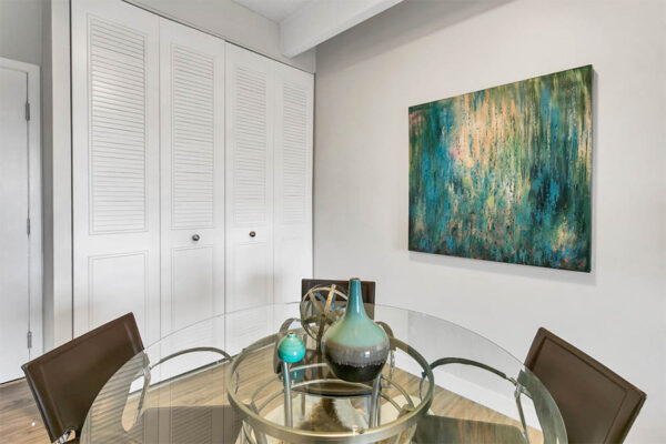 Dining room with glass dining table and chairs, abstract artwork, and closet with slatted doors.
