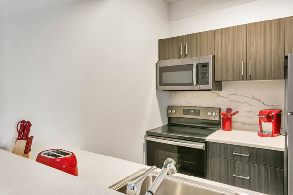 Kitchen with wood cabinets, light counters, stainless steel range and microwave, and red appliances.