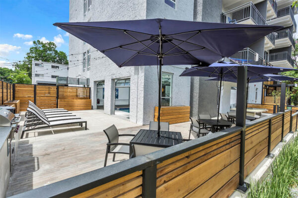 Outdoor patio with umbrellas, tables, lounge chairs, and garage doors to indoor pool.