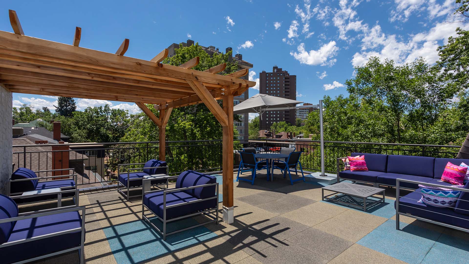 Rooftop patio with plush outdoor furniture, wood pergola, and metal railing overlooking Denver.