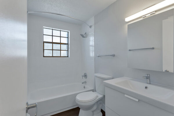 Bathroom with wood floor, white cabinets and counter, large mirror, and tiled shower.
