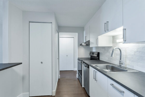 Kitchen with wood floor, white cabinets, dark counters, and stainless steel appliances.