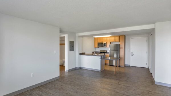 Living room with wood floor, white walls, grey trim, and kitchen with dining table.