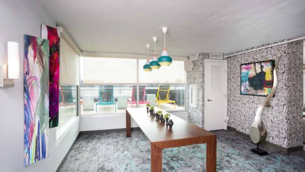 Lounge with carpet, large wood table, artwork, large metal sculpture, and large windows.