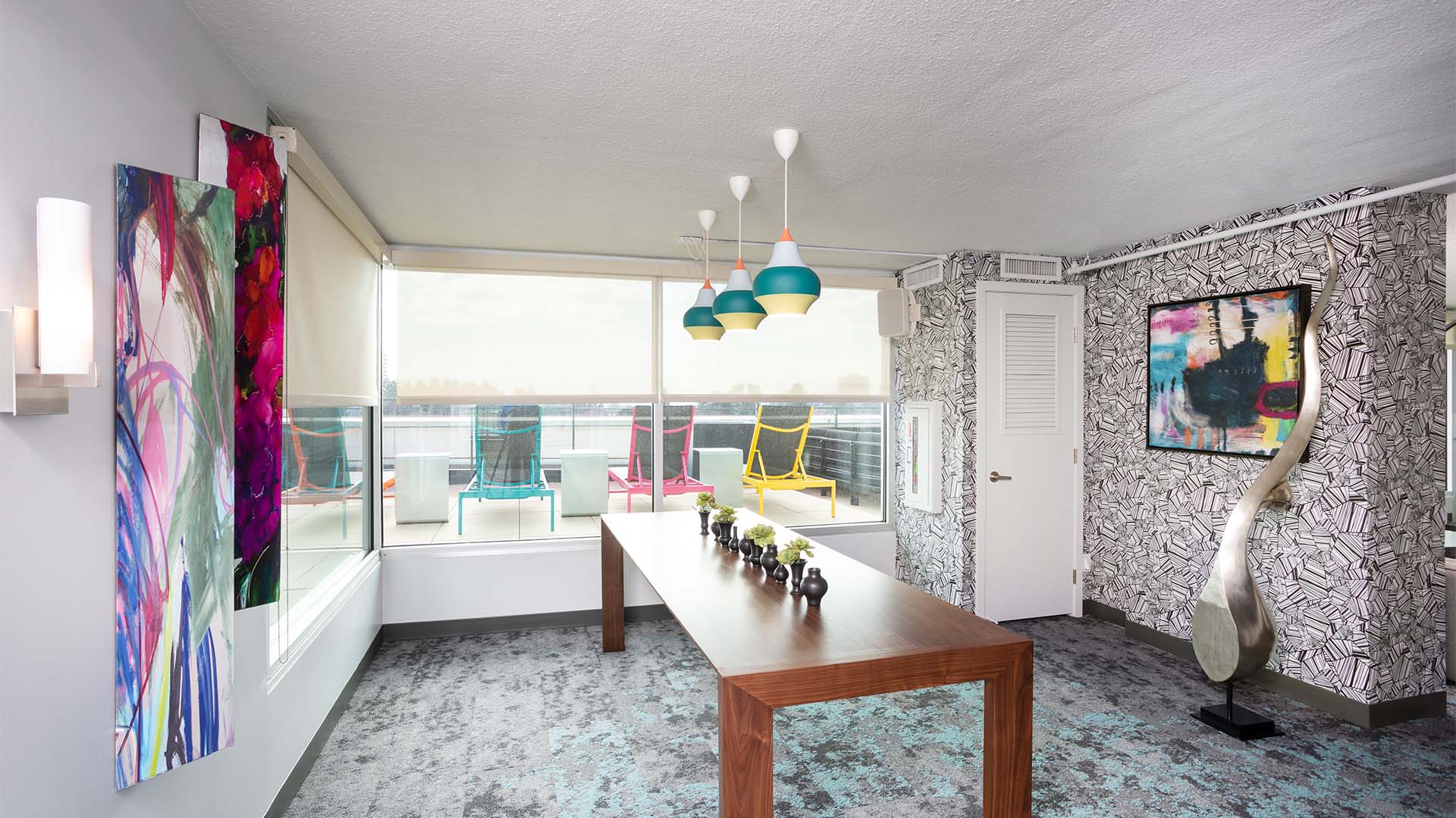 Lounge with carpet, large wood table, artwork, large metal sculpture, and large windows.