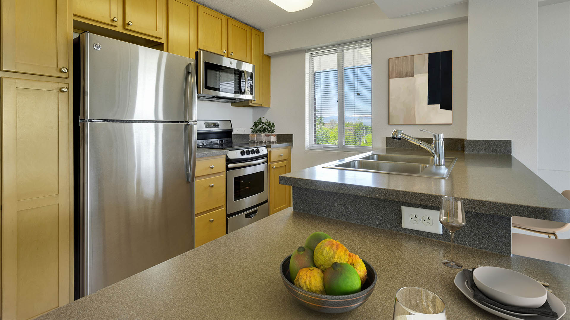 Apartment kitchen with stone counters, stainless steel appliances, and wood cabinets.
