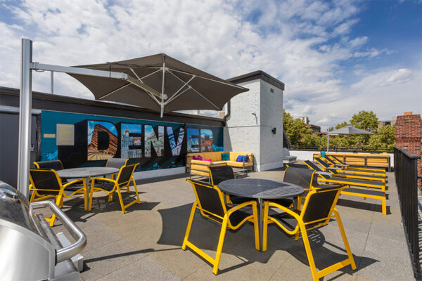Rooftop patio with lounge chairs, dining tables, large umbrella, and Denver mural.