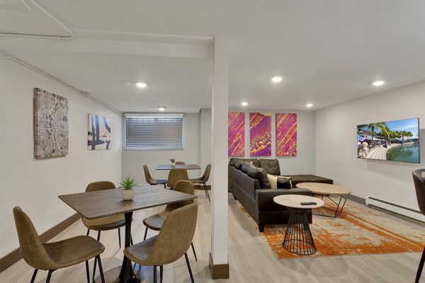 Lounge with wood floor, dining tables, plush sectional, and large TV.