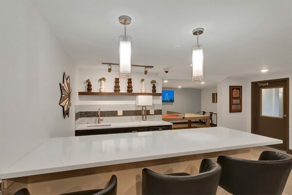 Demo kitchen with white counters, leather stools, wood decor, and lighting fixtures.