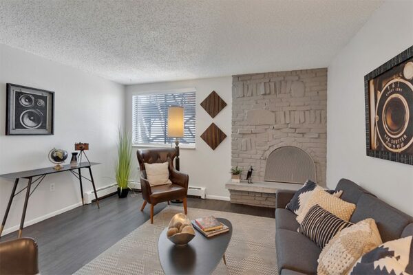Living room with wood floor, plush rug, comfortable seating, and brick accent wall with fireplace.