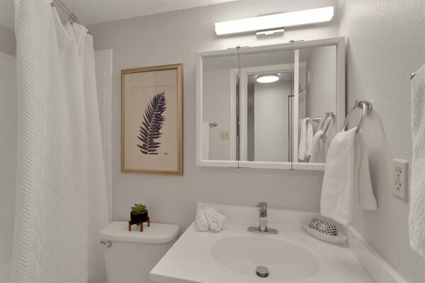 Bathroom with white counter, triple mirror cabinet, light fixture, and tiled shower tub.
