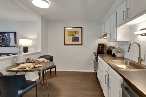 Kitchen with wood floor, white cabinets, dark counters, and stainless steel appliances.