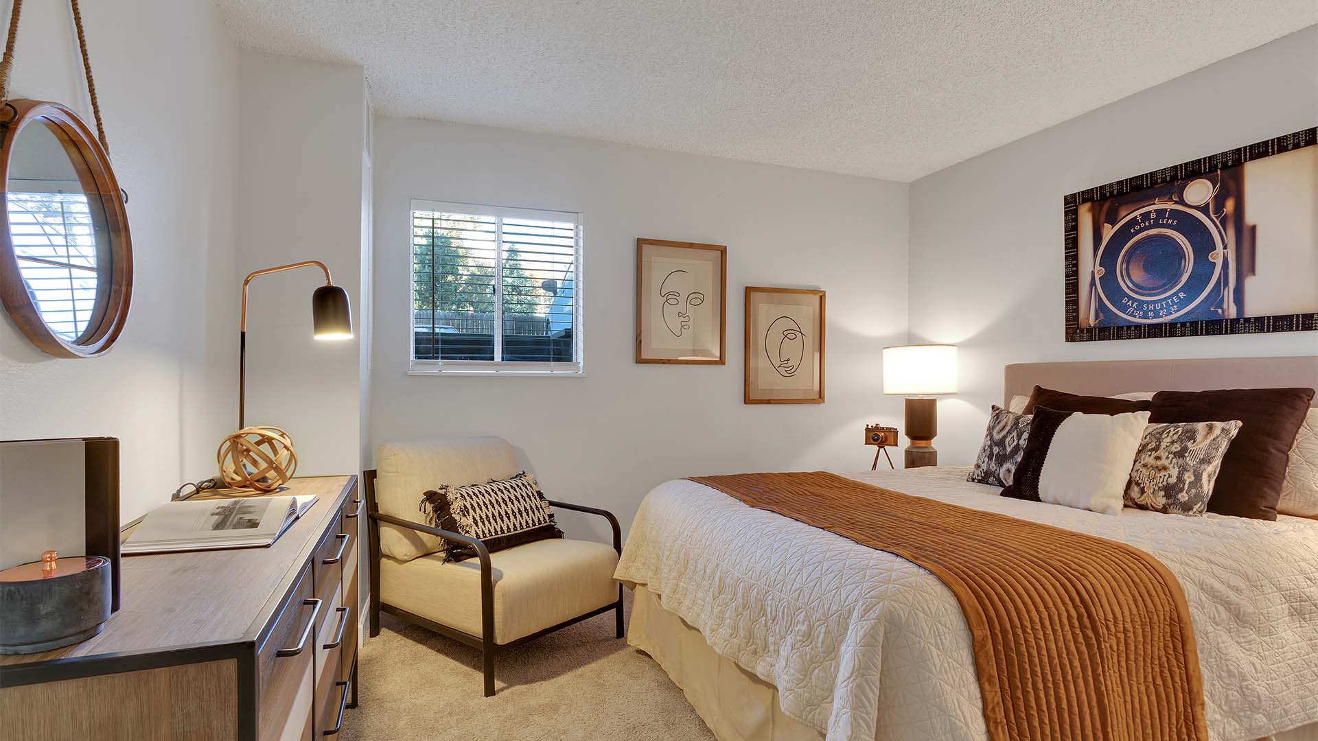 Bedroom with plush bed, wood dresser, framed artwork, and lounge chair.