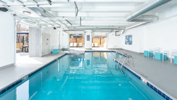 Indoor pool area with lounge chairs and garage doors to outside.