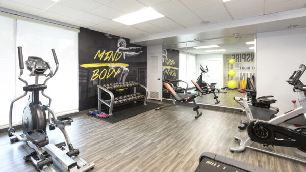 Fitness center with wood floor, mirror wall, dumbbell racks, and cardio machines.