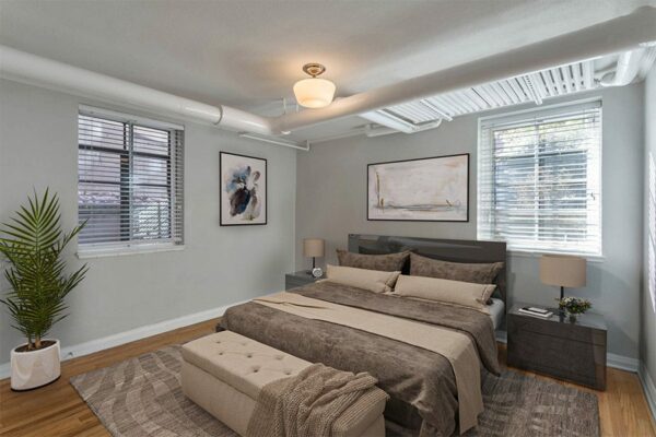 Bedroom with plush bed, bedside tables with lamp, and large windows.